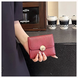 Detail of red litchi leather wallet featuring a round gold twist lock closure held by hand