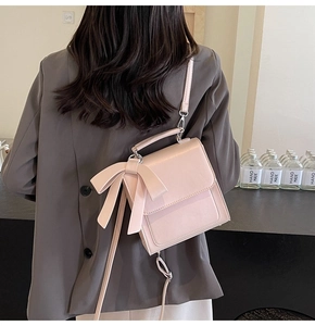 Pink faux leather handbag with a bow detail worn over a dark grey blazer for women