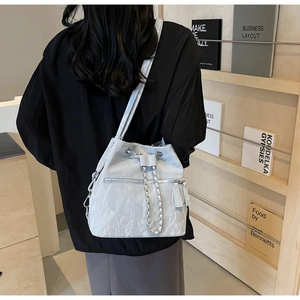 Close-up of light grey pleated bucket bag with silver chain and metal zipper details