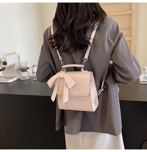 Detail of light pink PU leather backpack with bow accent shown in a cafe setting