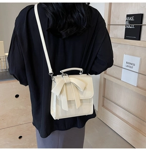 Rear view of model wearing a beige bow backpack with crossbody and handheld options