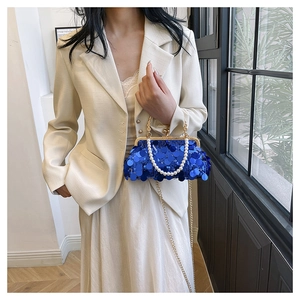 Modell trägt eine tiefblaue Pailletten-Clutch mit Perlengriff und Goldkette