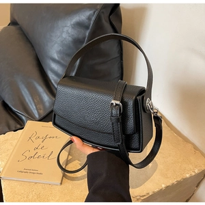 Detailed view of black litchi grain leather texture and silver buckle on a shoulder bag