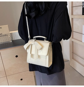 Detail view of cream crossbody bag with large bow decoration and adjustable strap