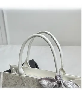 Detail of embroidered tote bag with rounded handle and decorative silk scarf accessory