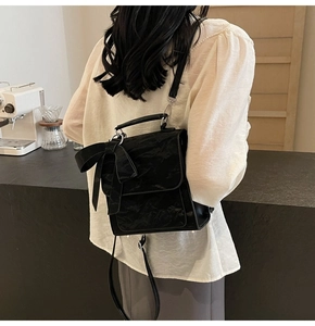 Detail of black pleated texture backpack featuring a large decorative bow on a cafe background