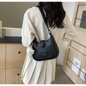 Détail d'un sac hobo en cuir noir avec lettrage doré et un porte-clé en peluche