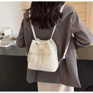 Rear view of a white glossy drawstring backpack with silver chain detail on model
