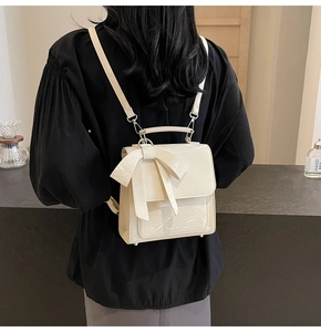Detail of cream white glossy leather backpack with a large bow showing the back-carrying style