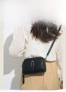Close-up of black litchi pattern camera bag with silver U-shaped metal buckle on model