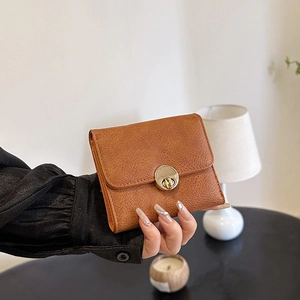 Brown textured leather wallet with gold twist lock shown in a minimalist lifestyle setting