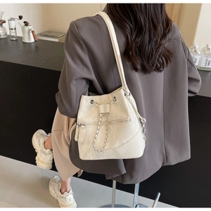 Macro shot of cream bucket bag showing glossy leather texture and chain drawstring detail