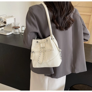 Lifestyle shot of cream white drawstring bucket bag with silver chain on model in cafe