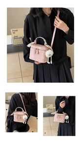 Detail view of a pink box-style bag with silk scarf handle and plush pom-pom charm