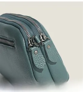Detailed macro of pebble leather texture and sturdy dual metal zippers on crossbody bag