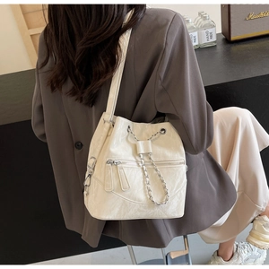 Detail of white textured bucket bag featuring silver chain drawstring and front zipper pockets