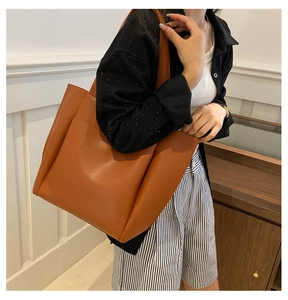 Close-up of a brown leather tote bag with large front pocket on a model's shoulder