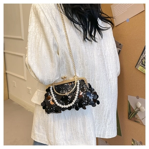 Detail der schwarzen Pailletten-Abendtasche mit Perlengriff und Goldkette auf weißem Blazer
