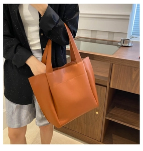 Detail of a large brown faux leather tote bag with open front pocket and shoulder straps
