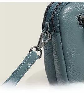 Detail of dual metal zippers and textured lychee leather on a dark teal shoulder bag
