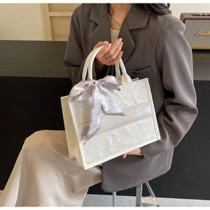 Detail of white embroidered tote bag with floral patterns and silk scarf accessory