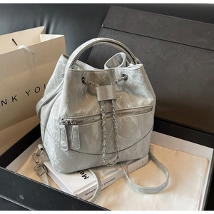 Detailed view of grey pleated bucket bag with metal chain drawstring and dual front zippers