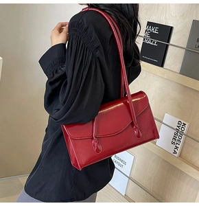 Side view of a bright red glossy PU leather shoulder bag with double straps on a model
