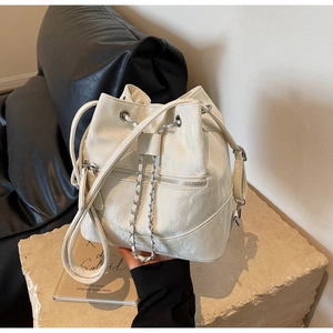 Detail of cream drawstring bucket bag with pleated texture and metal chain accent