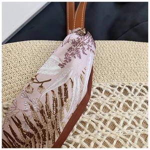 Détail d'un sac cabas en paille tressée avec foulard en soie et poignée à surpiqûres