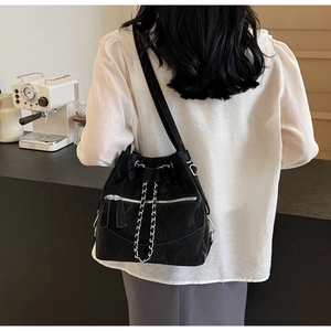 Close-up of a black bucket bag with silver chains in a cafe setting worn by a model