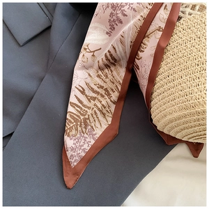 Détail d'un foulard en soie à motif feuilles avec bord contrasté sur un sac en paille