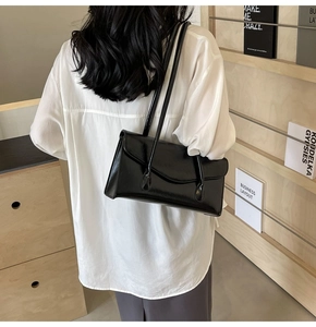 Detail of a minimalist black glossy underarm bag with sleek thin straps on a model