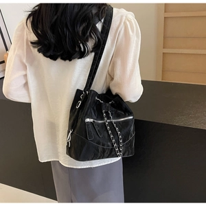 Detail of a black bucket bag showing glossy pleated texture and silver chain drawstring