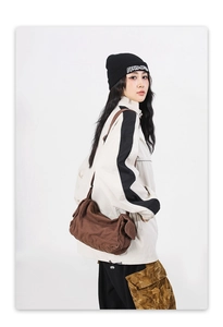 Close-up of a large brown canvas messenger bag with flap shown on a model