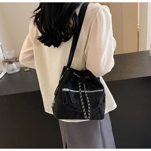 Detail of black bucket bag with silver zippers and chain strap worn by a model