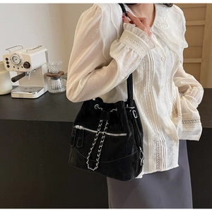 Detail of black drawstring bucket bag with silver chains and front pockets in cafe setting