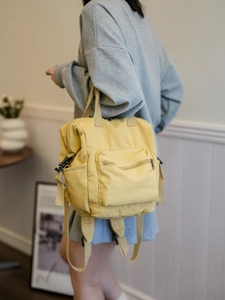 Detail of yellow canvas backpack with multiple pockets and top handle shown in a minimalist room