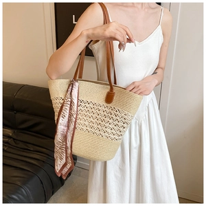 Detail of beige woven straw tote bag with brown leather handles and decorative silk scarf