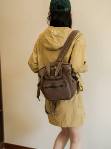 Detailed view of a dark brown canvas backpack with large front pocket and top handle