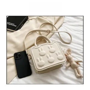 Detail view of cream white crossbody bag with embossed bunny motifs and shoulder strap