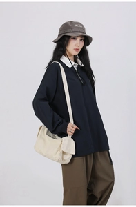 Detail of a minimalist off-white canvas crossbody bag styled with casual navy polo shirt