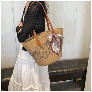 Détail d'un sac cabas en paille tressée avec motifs ajourés et un foulard en soie marron