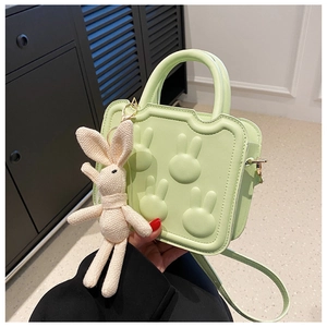 Close-up of mint green square bag with embossed rabbit design and white plush charm