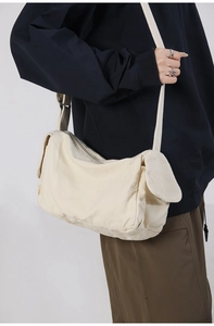 Model view of an off-white canvas crossbody bag featuring adjustable straps and fabric texture