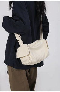 Detail view of the beige canvas messenger bag worn by a model in a casual studio setting