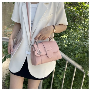 Close-up of pink litchi grain leather bag with decorative metal leaf pendant and strap
