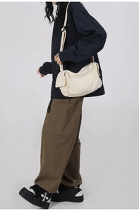 Side view of a cream-colored canvas crossbody bag worn by a model in a casual studio setting