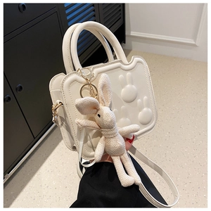 Detail of white bread-shaped handbag featuring 3D rabbit reliefs and a knit bunny charm