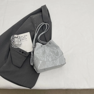 Minimalist light grey wrinkled bucket bag with chain strap on a grey blazer