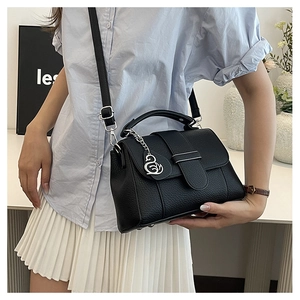 Close-up of black lychee-textured leather handbag with a silver swan pendant on a desk